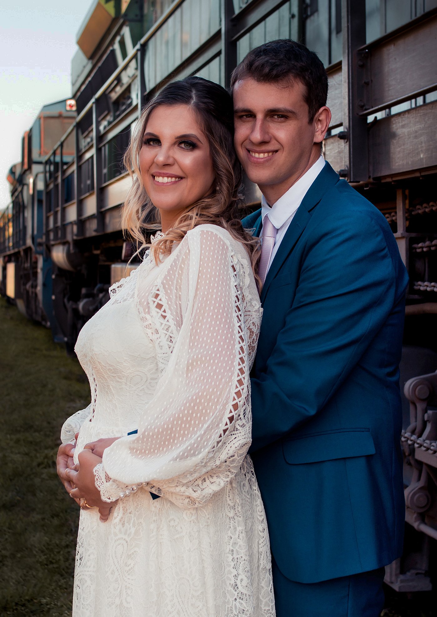 Anna e Felipe, noivos em Morretes, PR, sorrindo e abraçados com trem ao fundo.