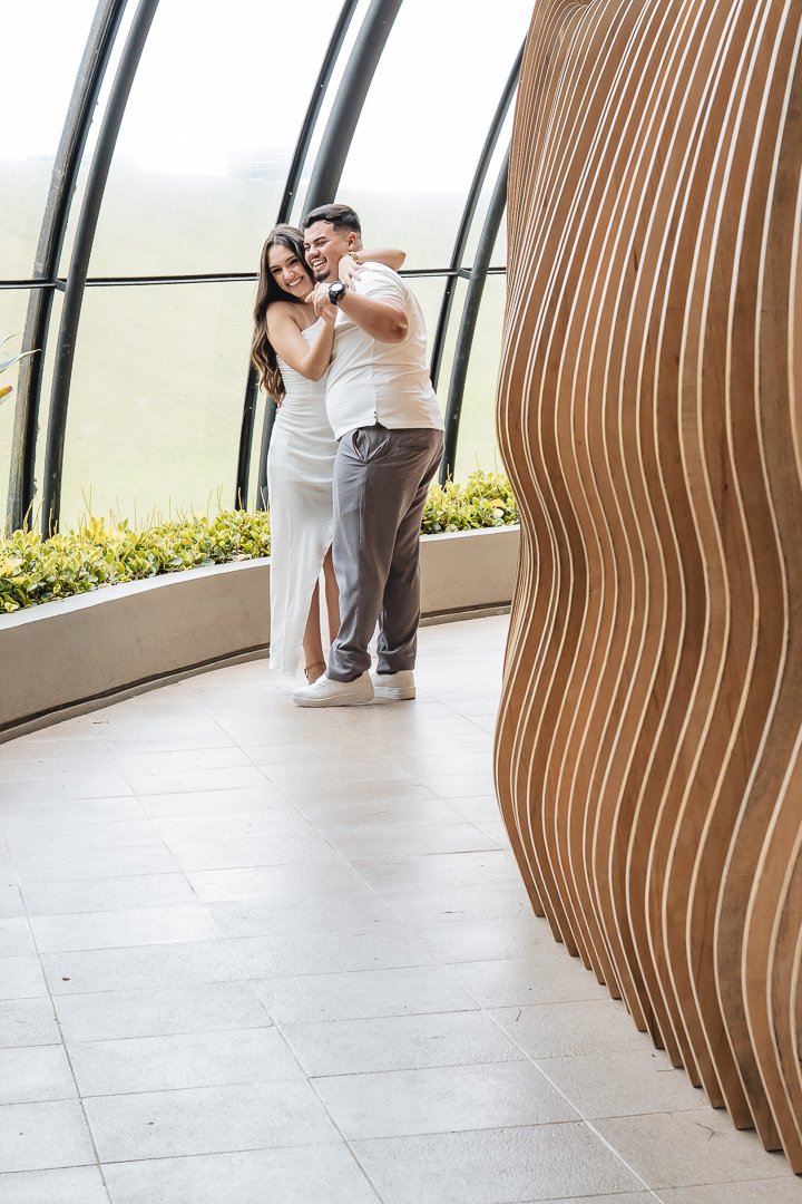 O casal se abraça em meio a risos na Galeria das Quatro Estações no Jardim Botânico de Curitiba.