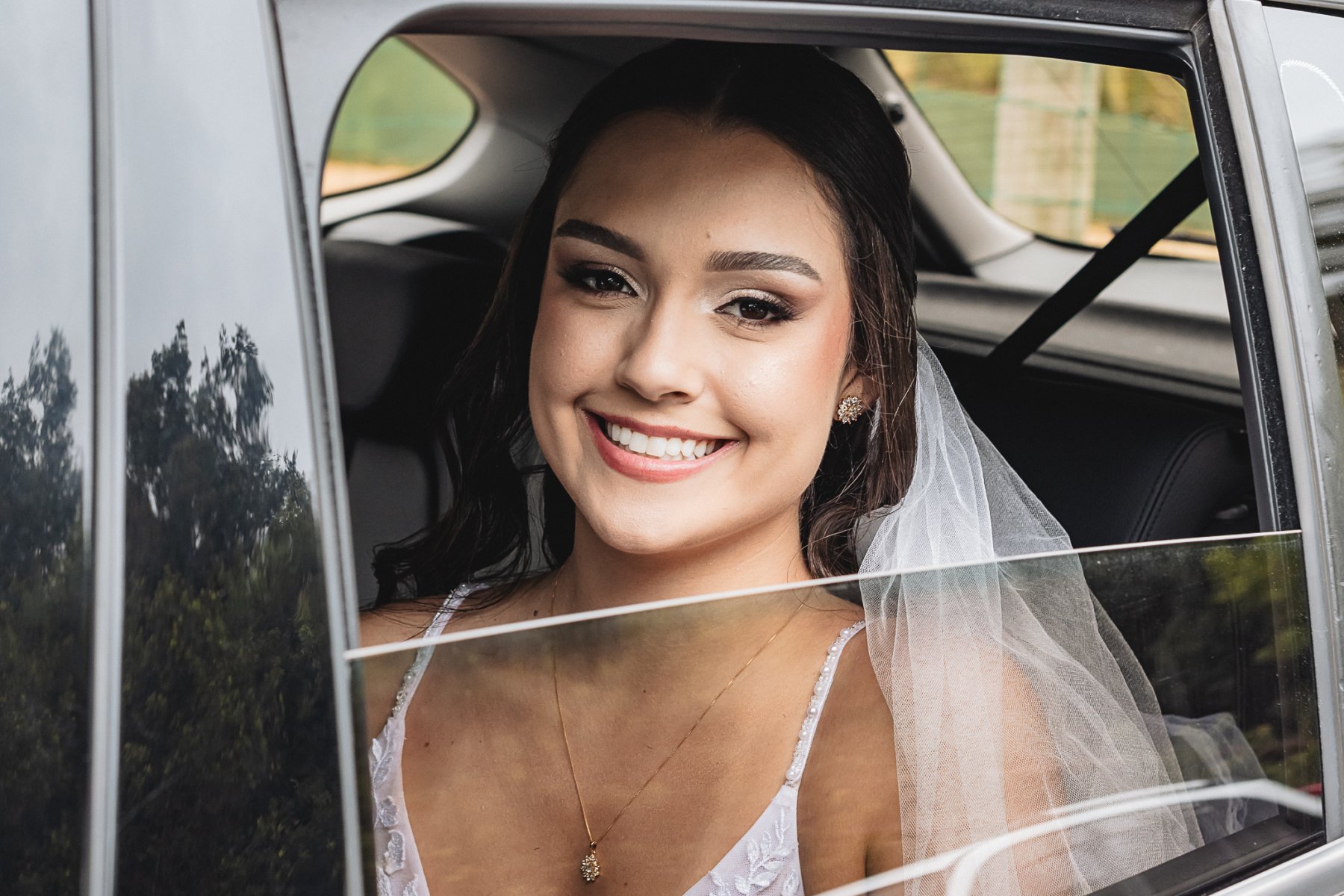 A noiva sorrindo na janela do carro na chegada a cerimônia.